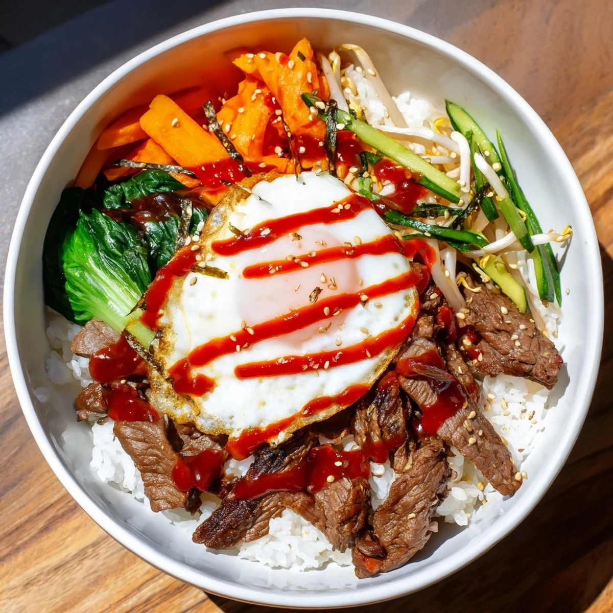 Korean-inspired breakfast bowl featuring savory beef, colorful julienned carrots, cucumber, and runny yolk over fluffy rice