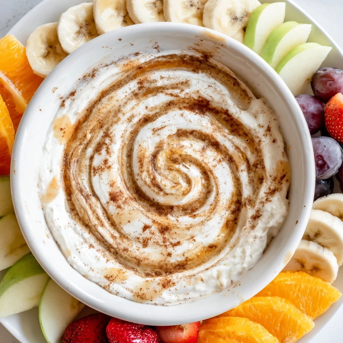 Protein-packed Greek yogurt cinnamon roll dip topped with cinnamon swirl and arranged fruit platter