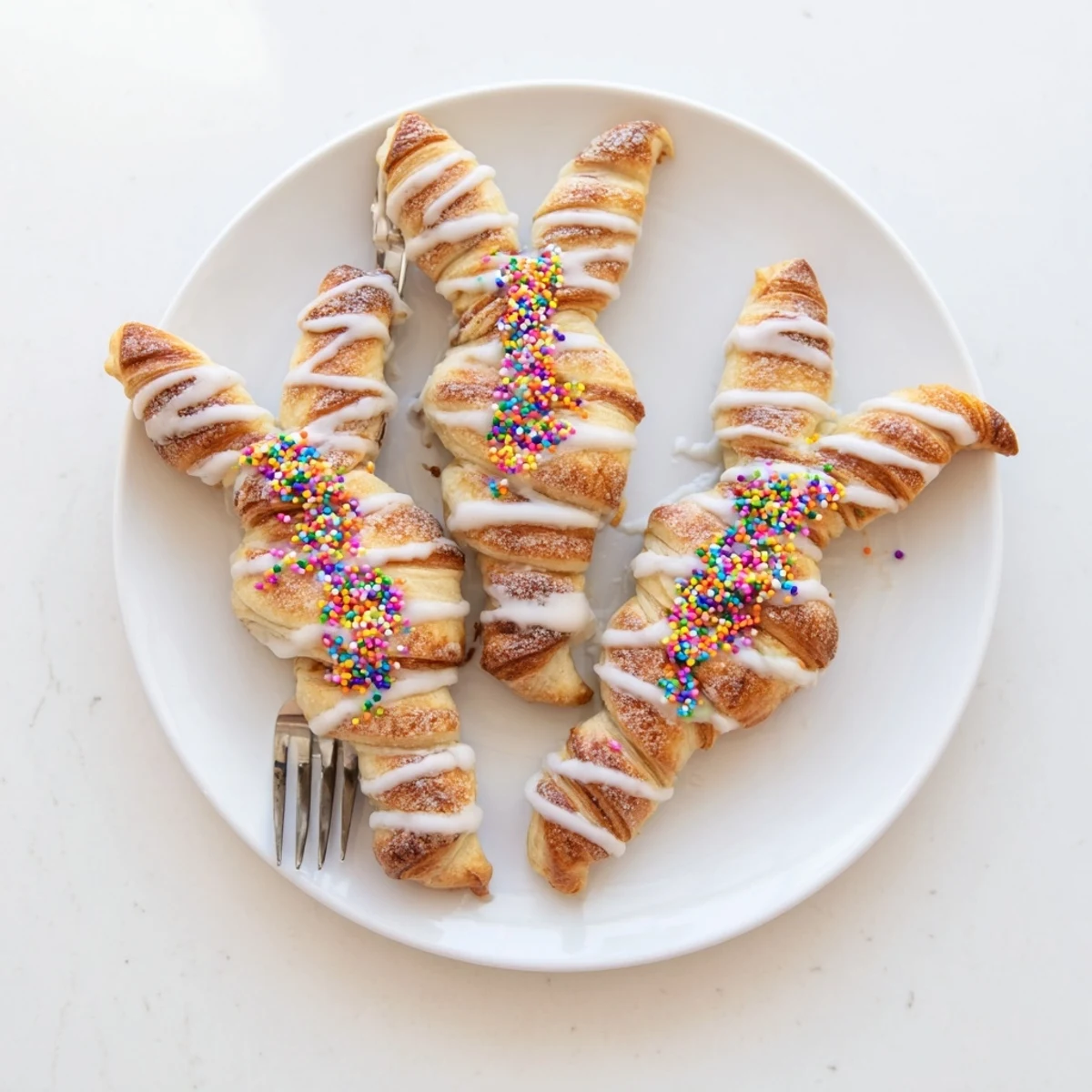 Golden Easter Bunny Twists drizzled with white icing and colorful sprinkles on a platter
