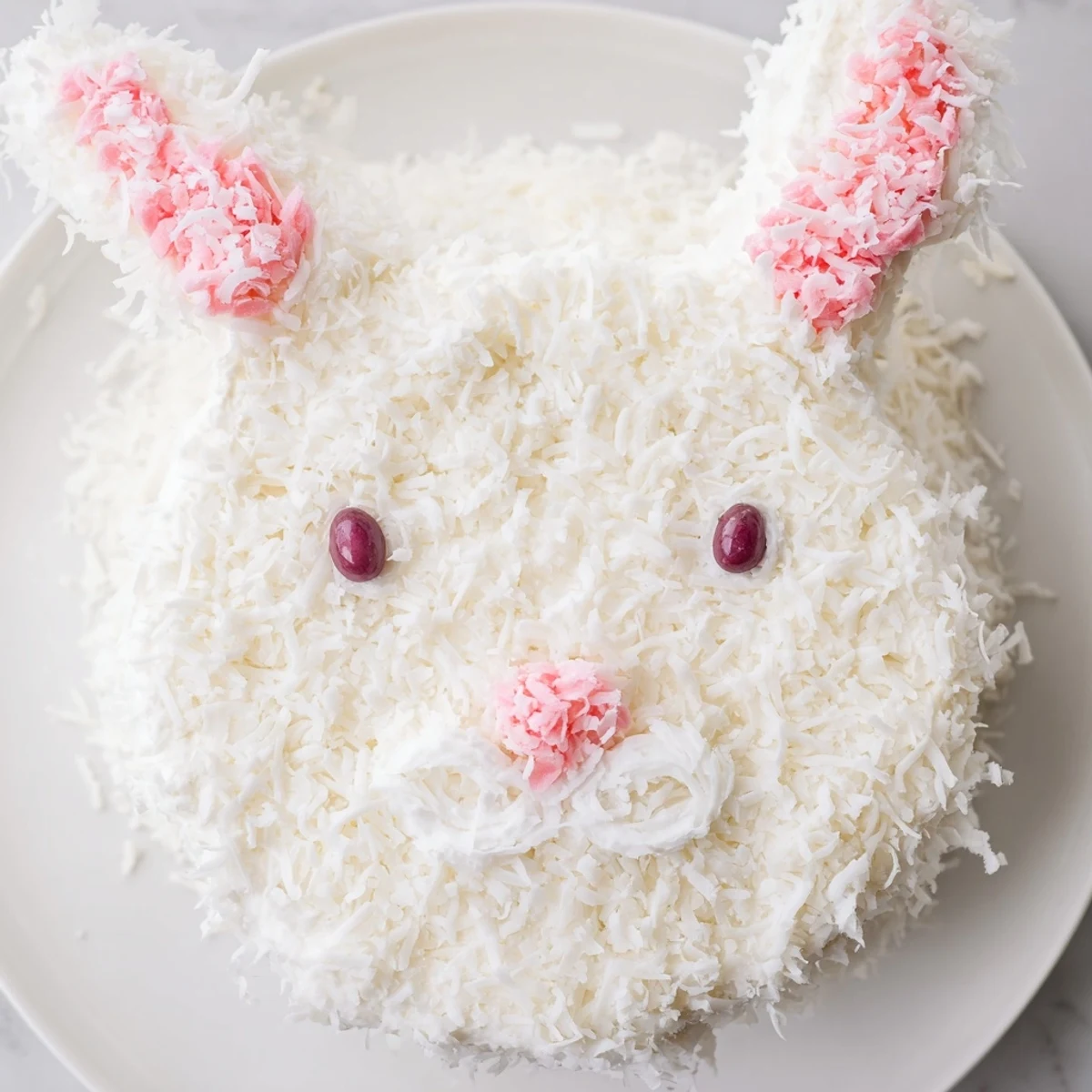 Festive bunny-shaped cake with pink coconut ears and candy face decorations for Easter celebration centerpiece