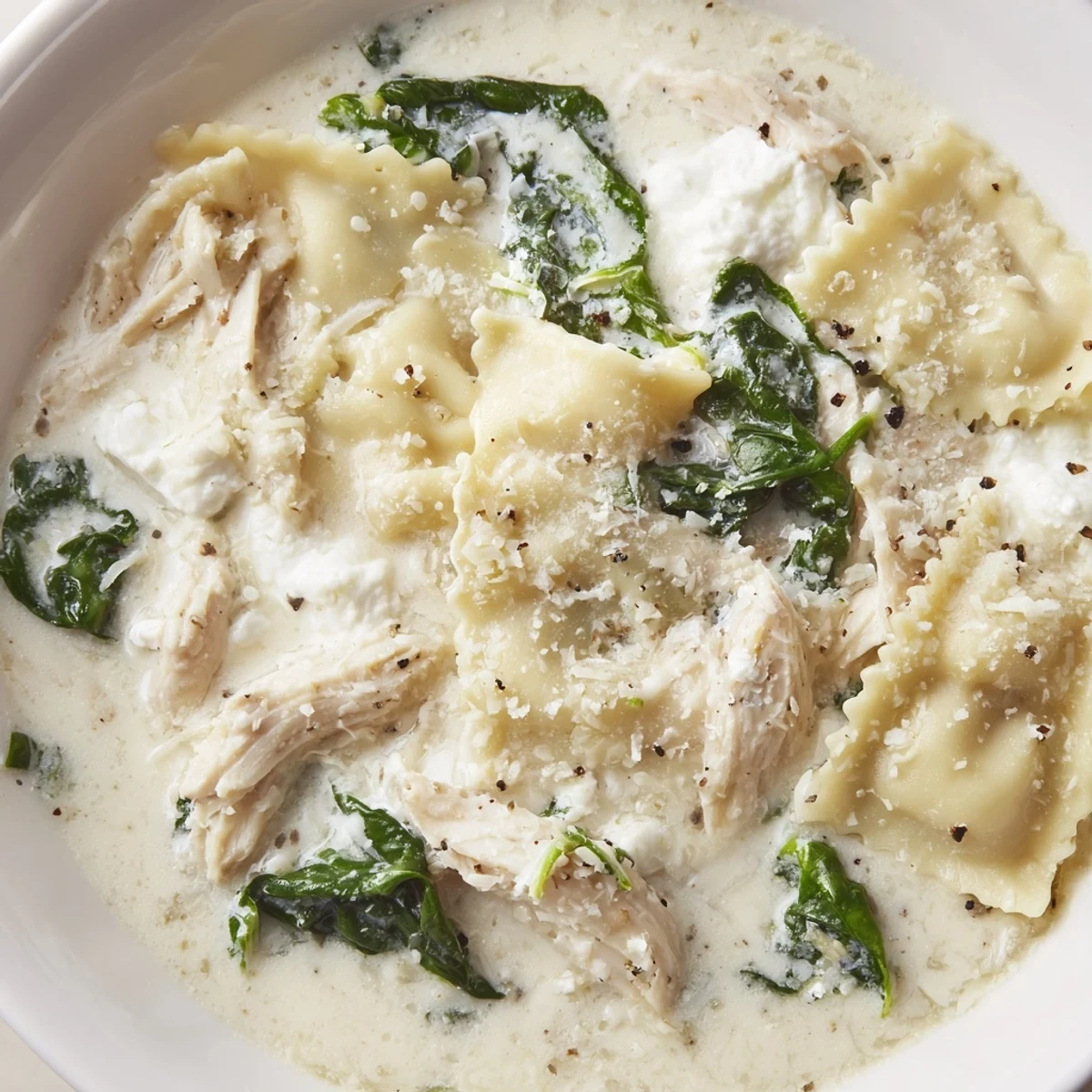 Steaming bowl of white lasagna soup topped with shredded chicken and fresh spinach