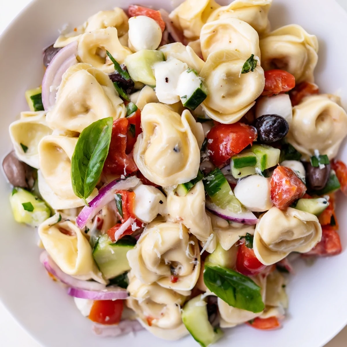 Colorful tortellini salad tossed with cherry tomatoes, cucumber, and zesty Italian dressing in a serving bowl