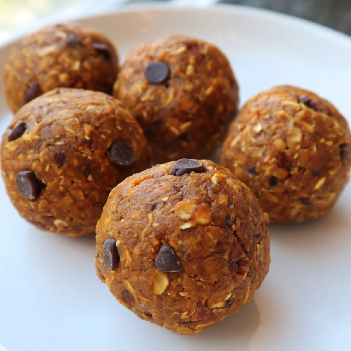 Golden no bake pumpkin protein balls studded with chocolate chips arranged on parchment for healthy meal prep