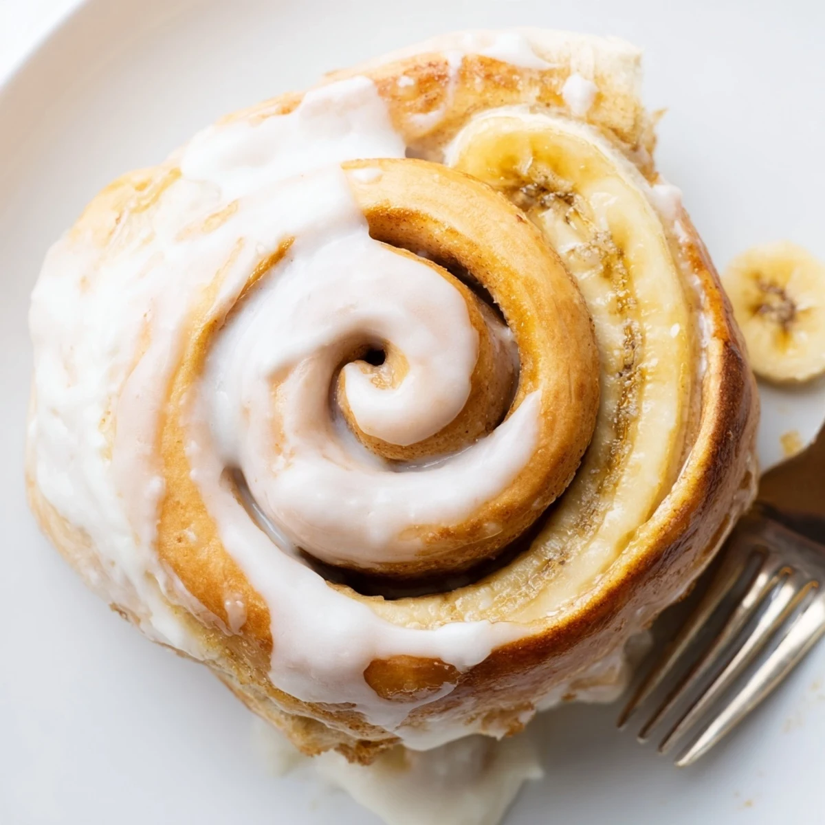 Homemade banana cinnamon rolls topped with vanilla cream cheese frosting on a wooden serving board