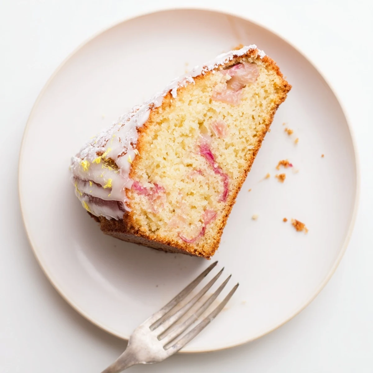 Golden rhubarb lemon drizzle cake with glistening icing and pink fruit pieces