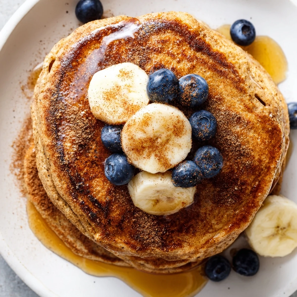 Golden stack of fluffy protein banana pancakes topped with fresh maple syrup and ripe banana slices