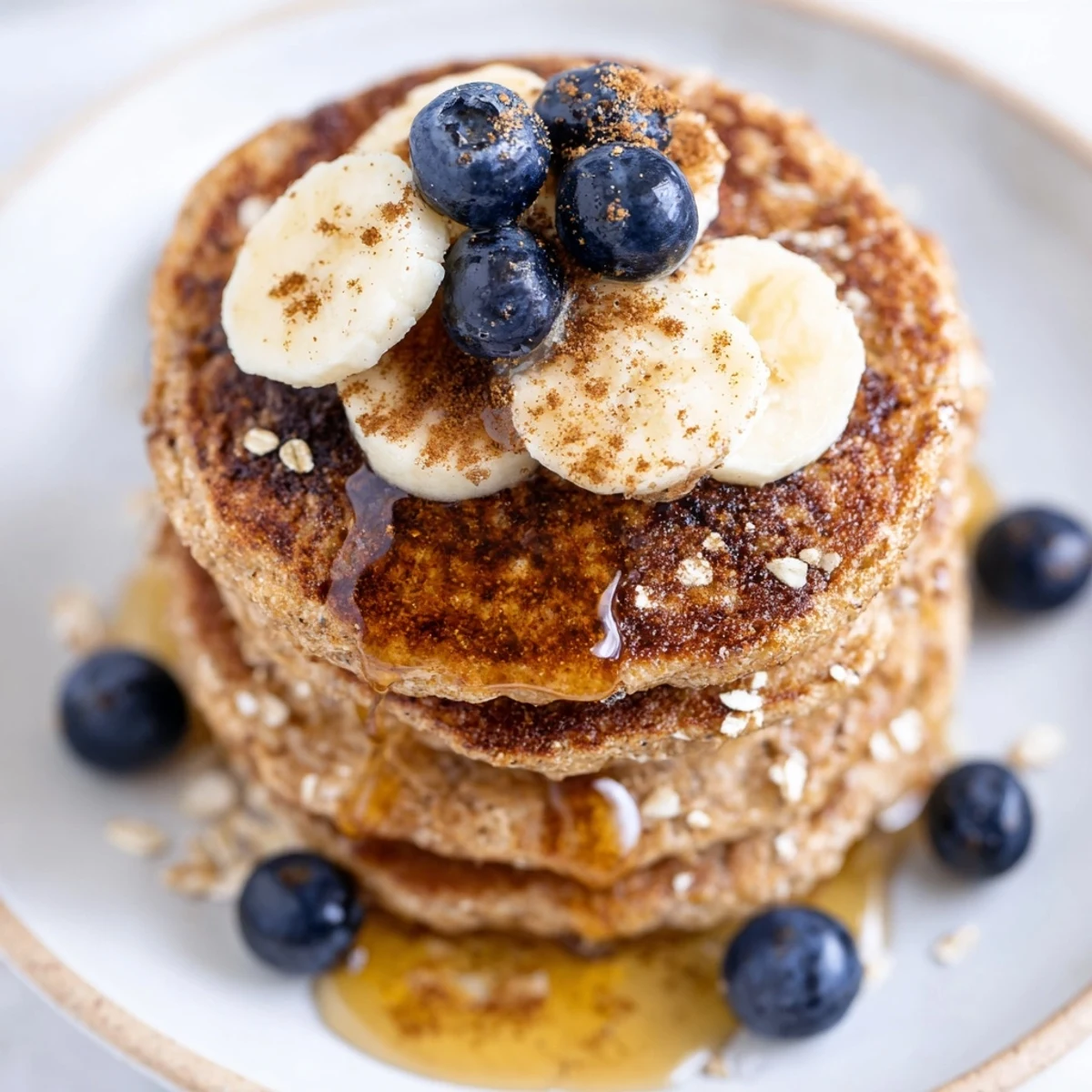 Homemade protein banana pancakes served on white plate with mixed berries and drizzle of honey