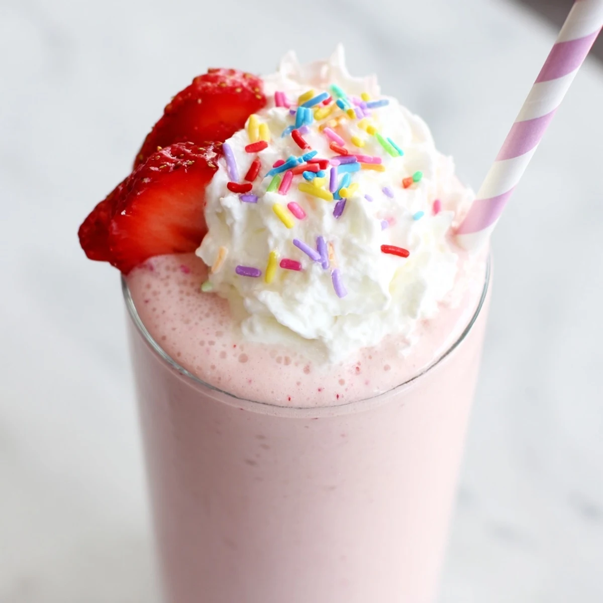 Creamy strawberry milkshake topped with whipped cream in a tall glass