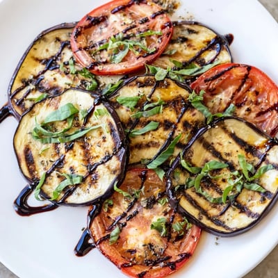 Tender charred grilled tomato eggplant drizzled with balsamic glaze and fresh basil